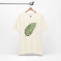 This T-Shirt features an illustration of a nephrolepis exaltata leaf, giving off a trendy and nature-inspired vibe. It is perfect for those who enjoy botanical prints and want to add a touch of greenery to their wardrobe. Ideal for casual wear or as a statement piece for nature lovers. Relevant for Earth Day, nature-themed events, and everyday leisure wear. Product features - 100% Airlume combed and ring-spun cotton - Retail fit for casual and semi-formal settings - Side seams for structural support - Ribbed knit collar with seam for elasticity - Shoulder tape for stability Care instructions - Machine wash: cold (max 30C or 90F) - Non-chlorine: bleach as needed - Tumble dry: low heat - Iron, steam or dry: medium heat - Do not dryclean Botanical Screen Print Short Sleeve T-shirt, Botanical Screen Print Crew Neck T-shirt, Crew Neck Cotton T-shirt With Plant Details, Cotton Crew Neck T-shirt With Plant Details, Cotton Crew Neck T-shirt With Plants, Cotton T-shirt With Plant Detail, Short Sleeve, Green Relaxed Fit T-shirt With Plant Detail, Green Botanical T-shirt With Graphic Print, Botanical Green T-shirt With Graphic Print