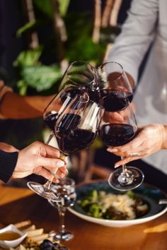 three people toasting with red wine at a dinner table