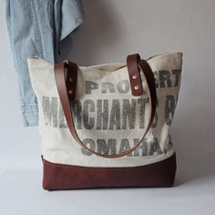 There's nothing better than the texture and patina of a 1940s-era flour sack.  This flour sack was stamped, "Property of Merchant Biscuit Co, Omaha, Nebr".  To craft it into a handbag the bold lettering was split in two to produce the front and back of the carryall.  The handles and bottom of the bag were made with premium chestnut brown leather cowhide that was top-stitched along the edge. American Harvest Bag Co designs the interior linings of their bags to "fit" into the exterior of the bags. Dark Abyss, Handcrafted Bags, Linen Canvas, Co Design, Chestnut Brown, Flour Sack, Chambray Shirt, Favorite Jeans, High Quality Leather