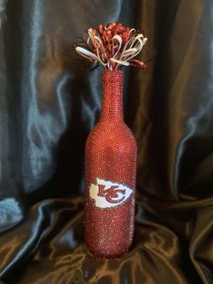 a red bottle with some flowers in it on a black cloth covered tablecloth background