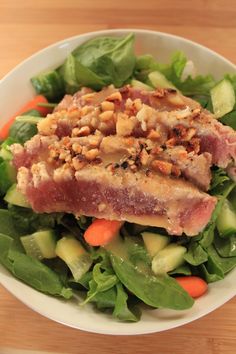 a white bowl filled with meat and vegetables on top of a wooden table next to a fork