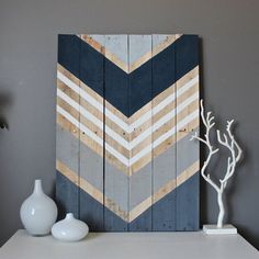 a white vase sitting on top of a table next to a wooden wall art piece