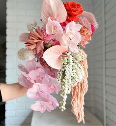 a person holding a bouquet of pink and red flowers in front of a brick wall