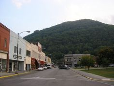 cars are parked on the street in front of some buildings and a large green mountain