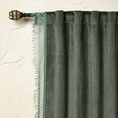 a green curtain hanging on the side of a white wall next to a metal hook