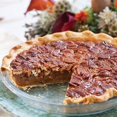 a pecan pie on a glass plate with one slice taken out and flowers in the background