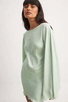 a woman wearing a green dress with long sleeves and an asymmetrical neckline