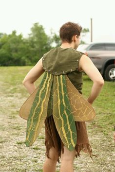 a man dressed up as a leaf fairy walking down a road with his back to the camera