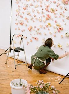 a woman kneeling down in front of a wall with flowers on it