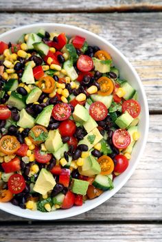 a white bowl filled with lots of veggies and avocado on top of a wooden table