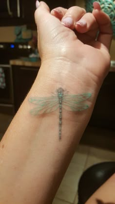 a woman's arm with a small dragonfly tattoo on the left side of her wrist