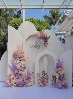 an outdoor ceremony setup with flowers on the wall and archway in the center, surrounded by palm trees