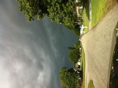 an empty road with dark clouds in the sky and trees on either side as well