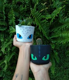 two hands holding up small pots with plants in them and eyes painted on the sides