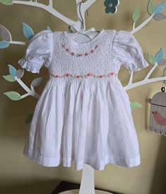 This dress is hand smocked in white.  Dainty embroidery around the front neckline and waist of the dress. Dress is fully lined with soft cotton material. The back closes with a zip and tie sashes.  This dress id made out of soft cotton fabric and lined in cotton fabric too. Suitable for kids with sensitive skin. 100% Cotton fabric Cold gentle machine wash Size 3-6 months (AU 00) Length 14" Chest circumference 20" Size 6-12 months (AU 0) Length 16" Chest circumference 21" Size 1  (12-18 months) Length 18" Chest circumference 22" Size 2 (18-24 months) Length 20" Chest circumference 23" Size 3 Length 22"  Chest circumference 24" Size 4  Length 24"  Chest circumference 25" Size 5   Length 26"  Chest circumference 26" Embroidered Fitted Baptism Dress For Summer, Cute Cotton Smocked Dress, White Smocked Dress With Smocked Bodice For Garden Party, White Dresses With Smocked Bodice, Fitted Smock Baptism Dress For Spring, Smock Dress For Baptism In Summer, White Smocked Dress For Baptism In Summer, Fitted Embroidered Baptism Dress For Summer, White Spring Dress With Smocked Cuffs