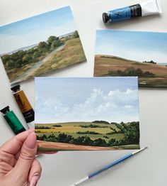 someone is holding up some paintings on the table