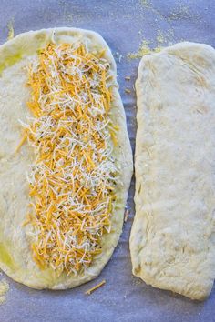 two uncooked pizza doughs with shredded cheese on the top and one rolled up