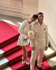 a man and woman standing on red carpeted stairs next to each other with flowers in their hands