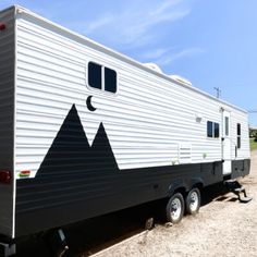 the trailer is parked on the dirt and has mountains painted on it's side