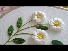 three white flowers with green leaves are on the embroidery pattern that is being worked on