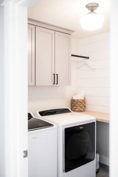 a washer and dryer in a white laundry room with cabinets on the wall