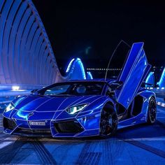 a blue sports car parked in front of a building at night with its doors open