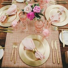 the table is set with gold plates and pink napkins, silverware, and flowers