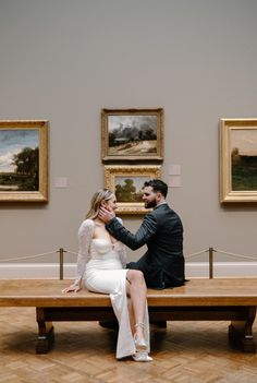 a man and woman sitting on a bench in an art gallery looking at each other