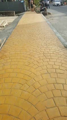 people are standing on the side walk next to a yellow brick sidewalk that has been paved with cobblestones