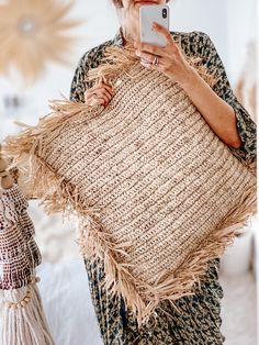 a woman taking a selfie with her cell phone while holding a large woven pillow