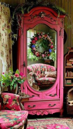 a pink armoire sitting in front of a mirror next to a chair and table