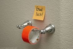 a toilet paper holder with an orange sticky note attached to it