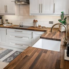 a kitchen with white cabinets and wood counter tops, an island sink and dishwasher