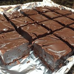 a piece of chocolate cake sitting on top of aluminum foil covered in frosting and cut into squares