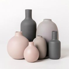 there are many different colored vases on the white table top, one is gray and the other is pink