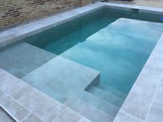 an empty swimming pool with steps leading up to the water and brick wall behind it