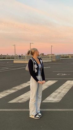 a woman standing in the middle of an empty parking lot with her hand on her hip