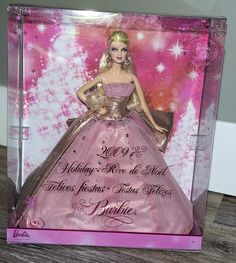 a barbie doll in a pink and gold dress is shown inside a plastic box on a wooden table