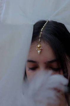 a woman wearing a gold head piece with pearls on it's forehead and feathers in front of her face