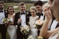 a group of people standing next to each other wearing tuxedos and holding bouquets