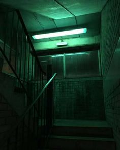 an empty stairwell in a dark building with green light coming from the ceiling and stairs