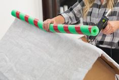 a woman holding a large green and red tube in her hand while standing next to a cardboard box