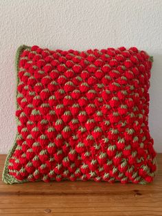 a red and green crocheted pillow sitting on top of a wooden table