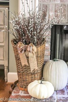 two white pumpkins sitting next to a wicker basket filled with branches and flowers