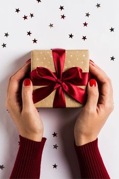 woman's hands holding a wrapped gift box with red ribbon and stars around it