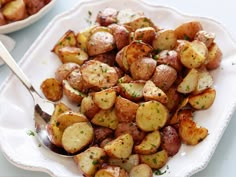 a white plate topped with potatoes covered in seasoning next to a bowl of sauce