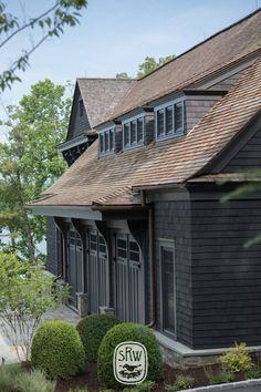 a black house with brown shingles on the roof and two large bushes in front of it