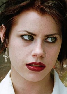 a woman with red lipstick and piercings looking at her cell phone in front of a graffiti wall