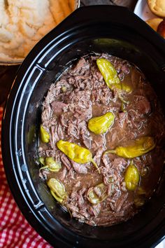 a crock pot filled with meat and peppers on top of a red checkered table cloth