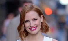 a woman with red hair wearing a white dress and pink lipstick smiling at the camera